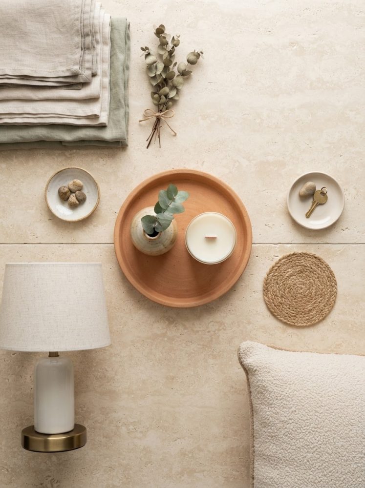 Conjunto decorativo minimalista com vela, vaso, almofada, luminária e têxteis em tons naturais