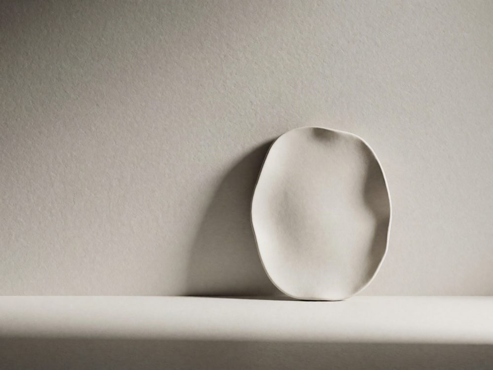 Prato cerâmico branco com forma irregular sobre fundo neutro com sombra suave