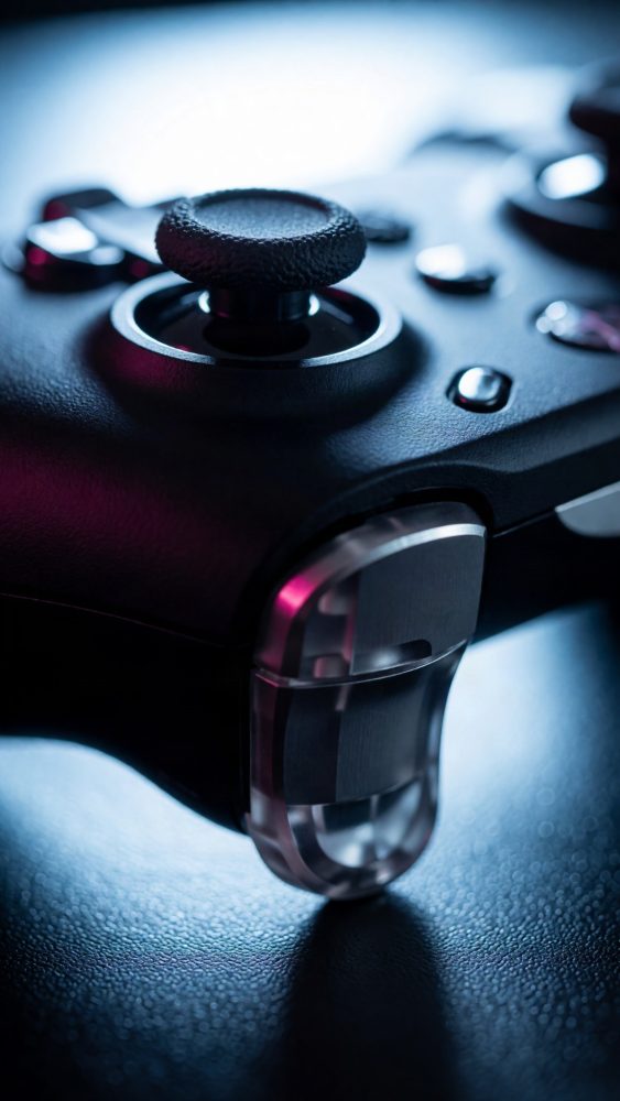 Controlador de videojogos preto iluminado com luz azul e rosa em fundo escuro