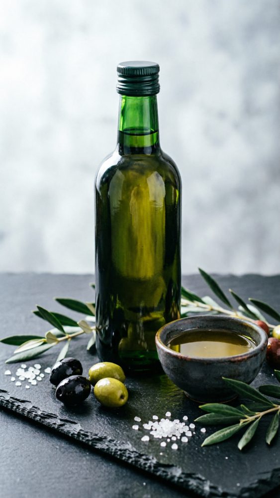 Garrafa de azeite verde com azeitonas, sal grosso e ramos de oliveira em ardósia preta