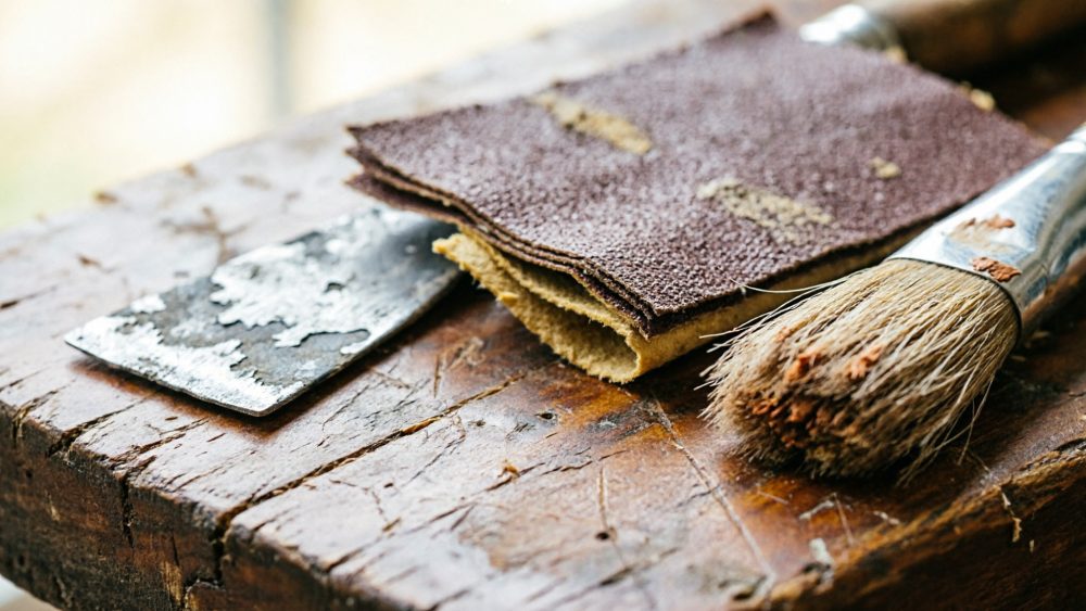 Ferramentas de restauração com pincel, lixas e espátula sobre superfície de madeira envelhecida