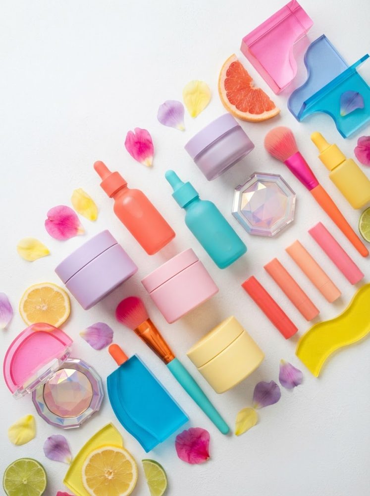 Cosméticos coloridos e acessórios com pétalas e frutas cítricas sobre fundo branco
