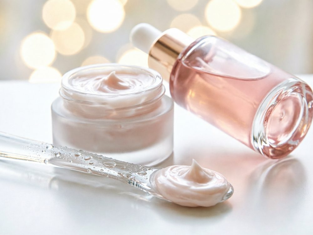 Frasco de creme branco, sérum rosa e espátula transparente com creme