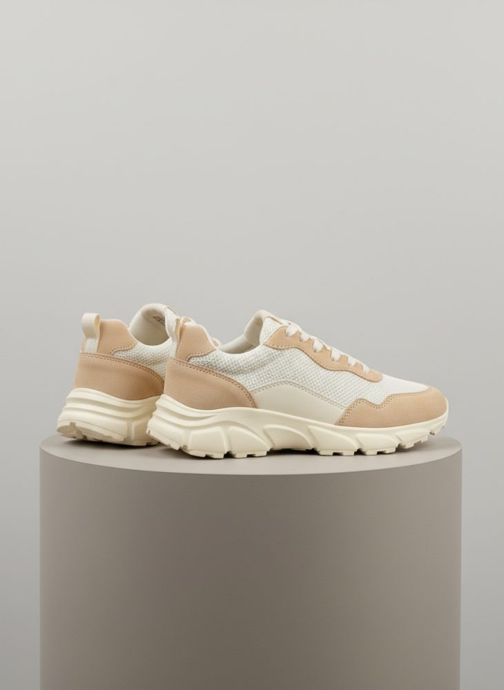 Par de tênis desportivos bege e branco com sola robusta sobre pedestal cinza