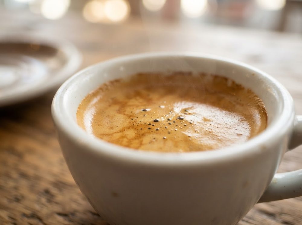 Chávena branca com café expresso quente e espuma cremosa sobre mesa de madeira rústica