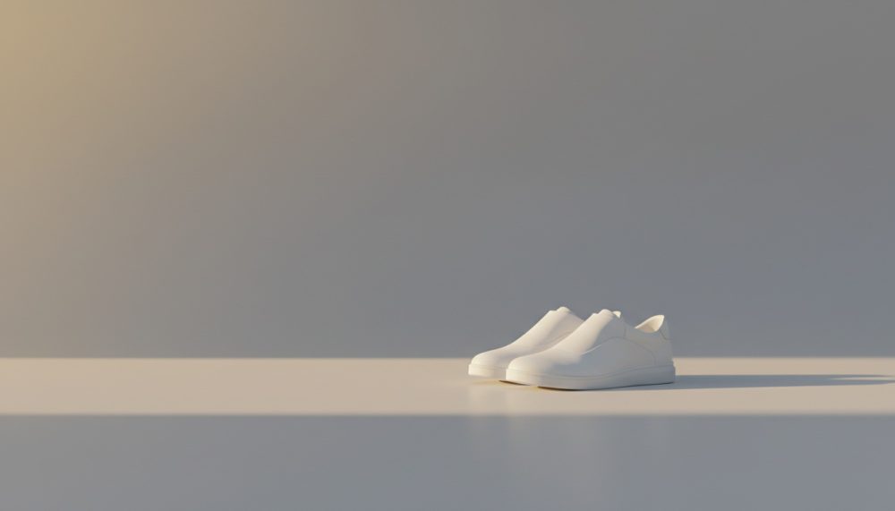 Ténis brancos minimalistas sobre superfície lisa com luz suave e sombras destacando o design moderno