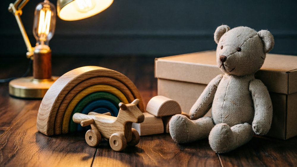 Brinquedos infantis de peluche e madeira sobre mesa iluminada com lâmpada amarelada