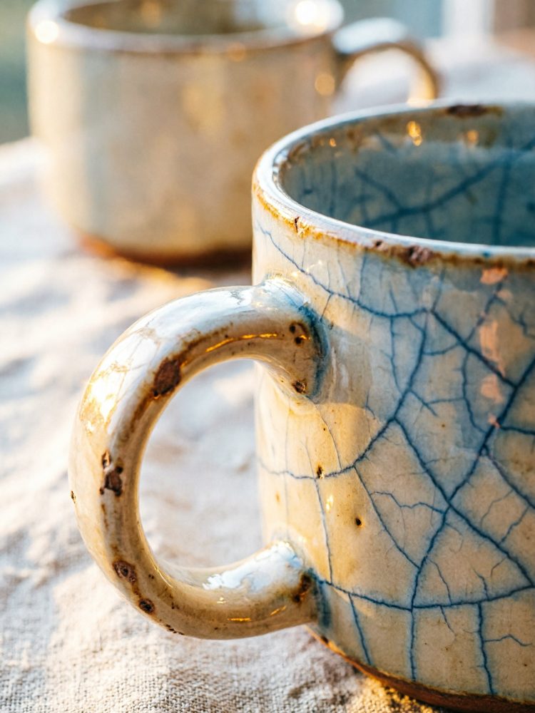 Close-up em alça de caneca cerâmica craquelada azul e bege com fundo desfocado