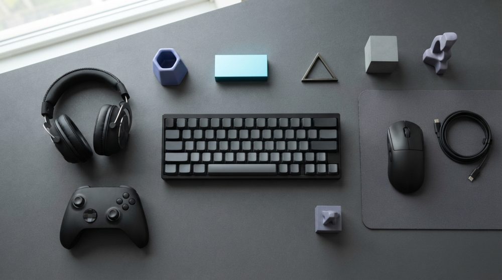 Conjunto de acessórios gaming modernos com teclado, comando, auscultadores e rato sobre mesa cinzenta