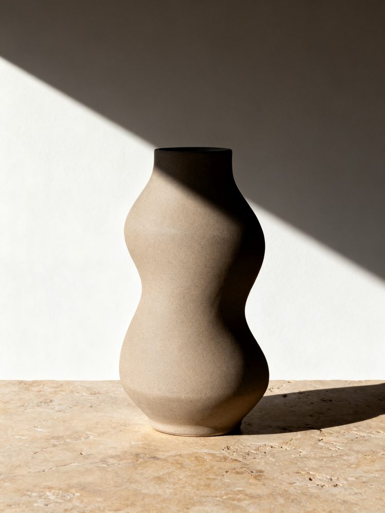 Vaso cerâmico beige com forma curva em luz natural sobre pedra clara