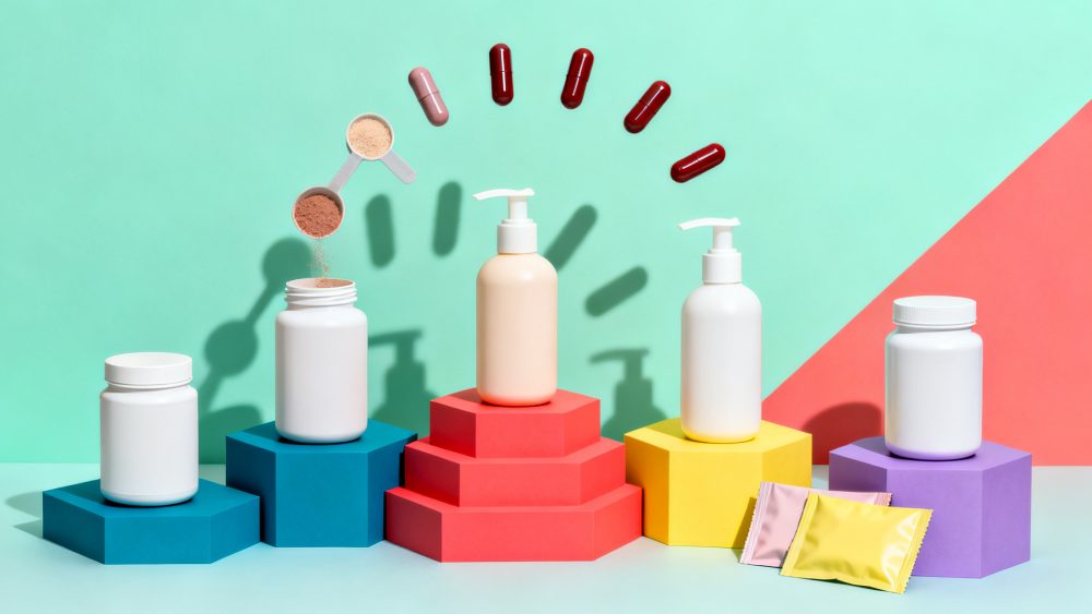 Frascos de suplementos e cremes em bases coloridas com cápsulas e pós em fundo verde e coral