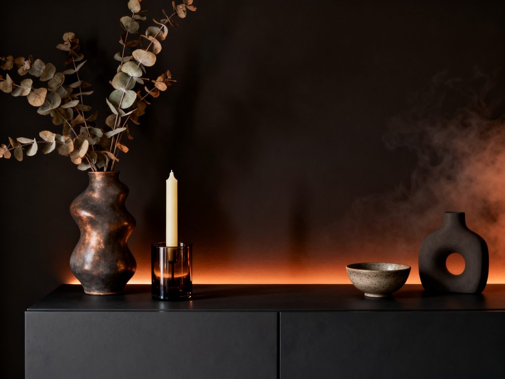 Vaso com ramos secos, vela, bowl e vaso preto em móvel com luz ambiente quente