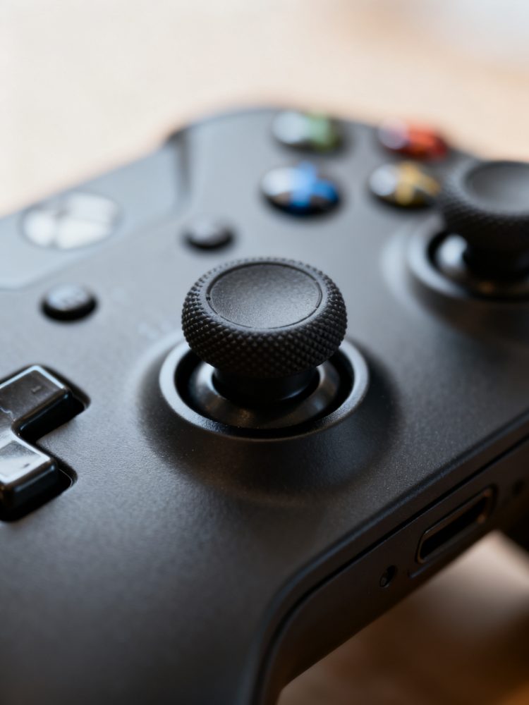 Comando de videojogo preto com joystick texturizado e botões coloridos em fundo claro