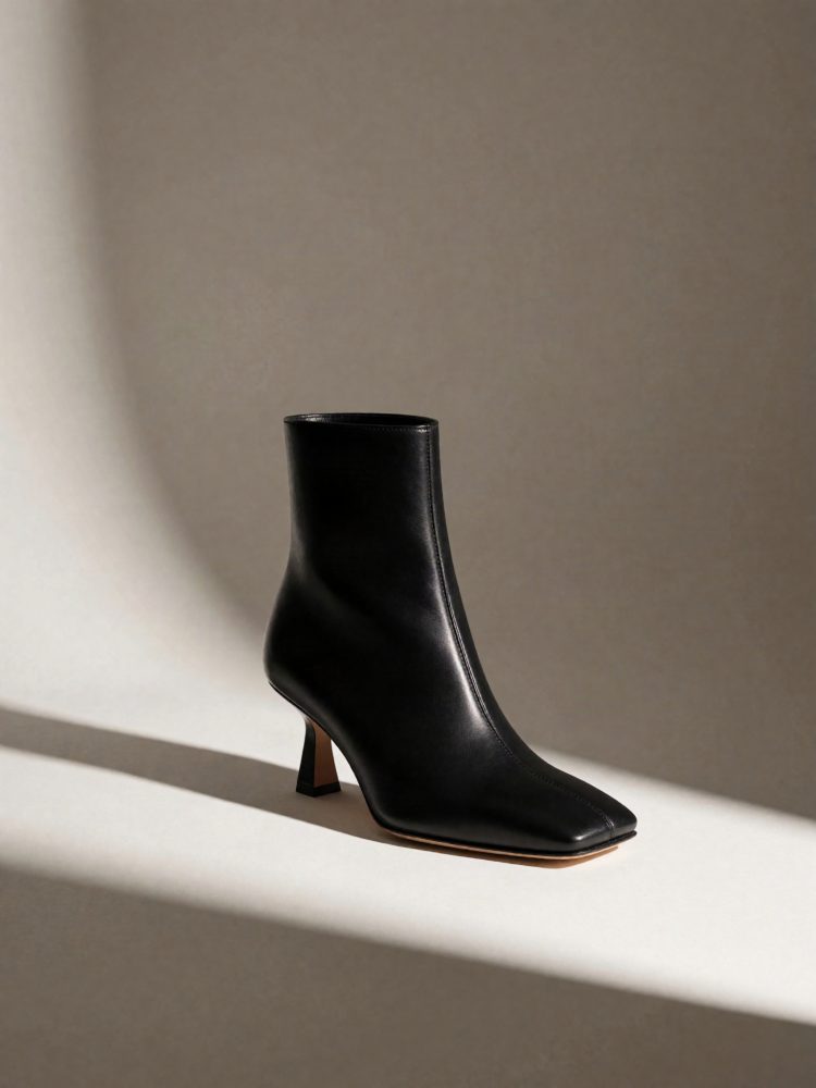 Botim feminino preto em pele com salto médio fino e bico quadrado, colocado em fundo neutro com iluminação suave