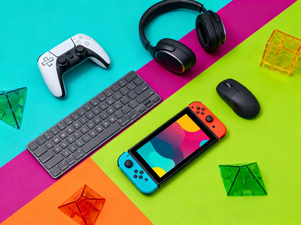 Acessórios gaming coloridos sobre fundo vibrante com teclado, comandos, auscultadores e rato