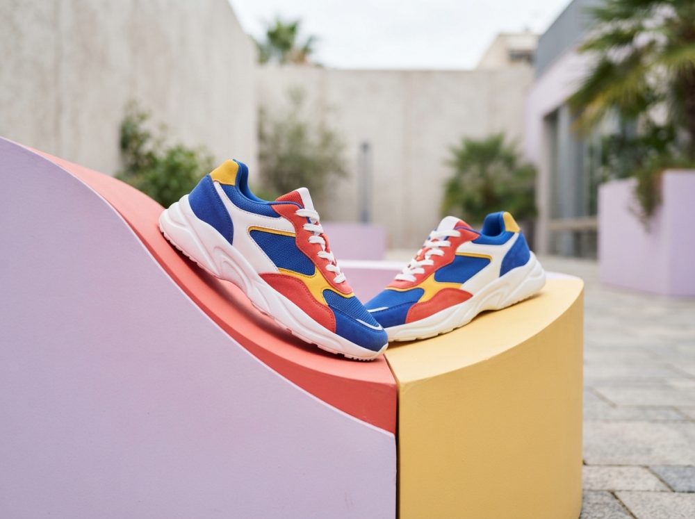 Ténis desportivos coloridos em azul, vermelho, amarelo e branco sobre bancos pastel curvos ao ar livre