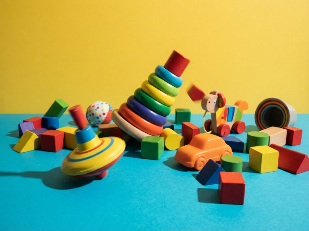 Brinquedos clássicos de madeira coloridos com formas geométricas e pião a rodar em fundo amarelo e azul