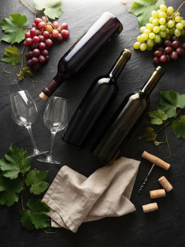 Garrafa de vinho, taças, uvas vermelhas e verdes, rolhas e saca-rolhas sobre mesa escura