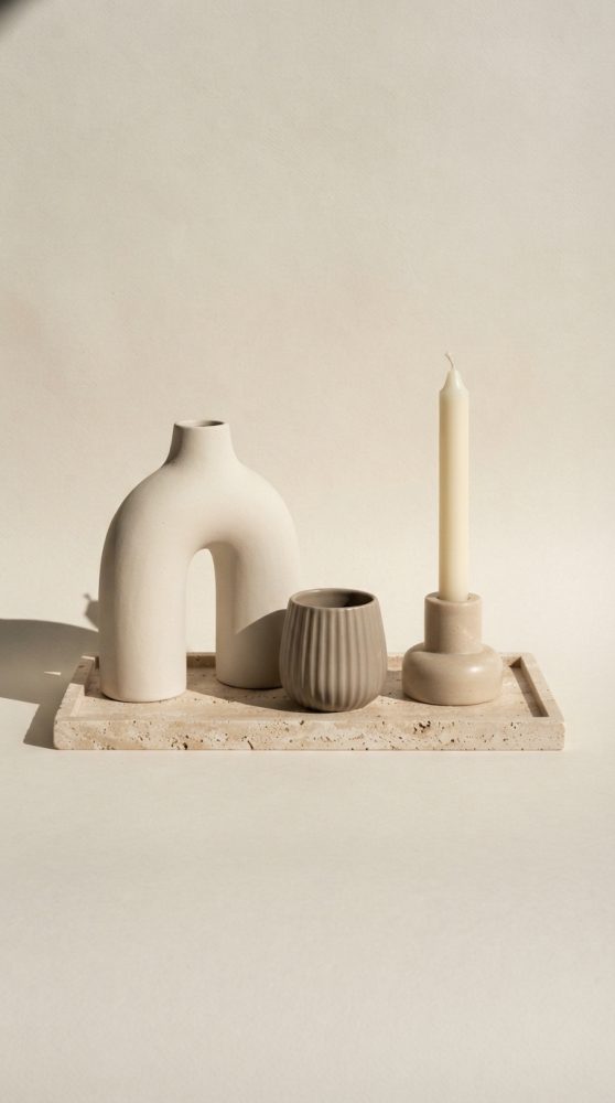 Conjunto de decoração minimalista com vaso arqueado, vaso texturizado e vela sobre base de pedra