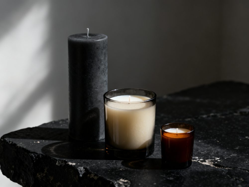 Três velas em diferentes recipientes sobre mesa escura sob luz natural suave