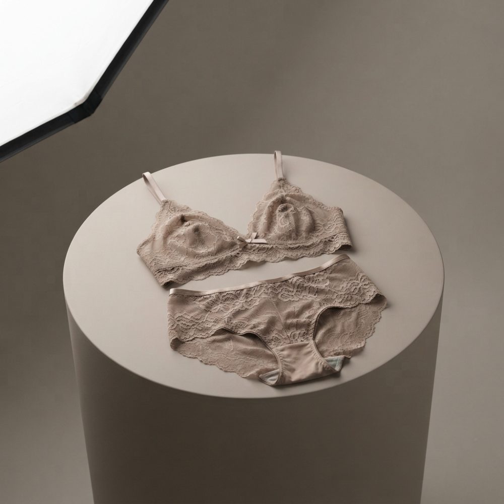 Conjunto de lingerie bege com renda delicada sobre cilindro branco em fundo neutro