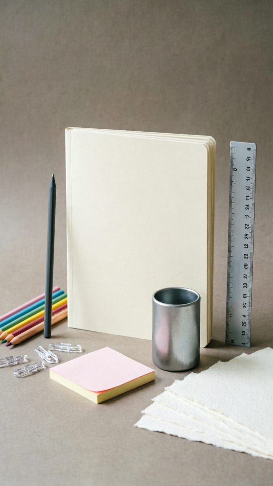 Conjunto de artigos de papelaria com caderno, lápis, blocos de notas, régua e clips sobre fundo neutro