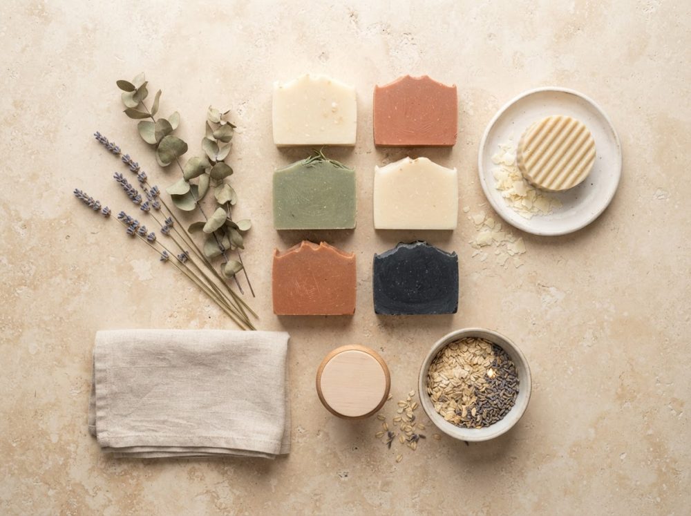 Seis sabonetes artesanais em tons naturais com lavanda, folhas secas e acessórios sobre superfície bege