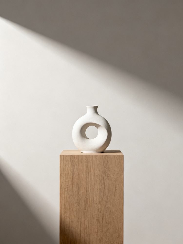 Vaso branco cerâmico circular com abertura no centro sobre pedestal de madeira clara