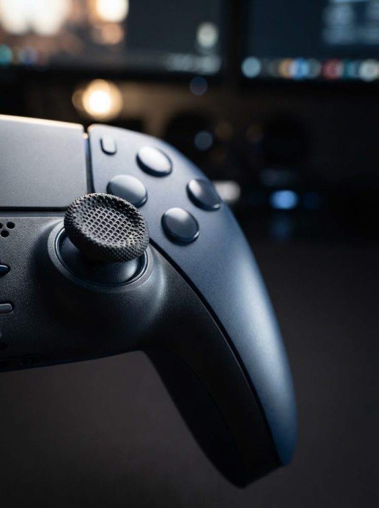 Comando de videojogo preto em close-up com botões e joystick texturizado ao fundo desfocado