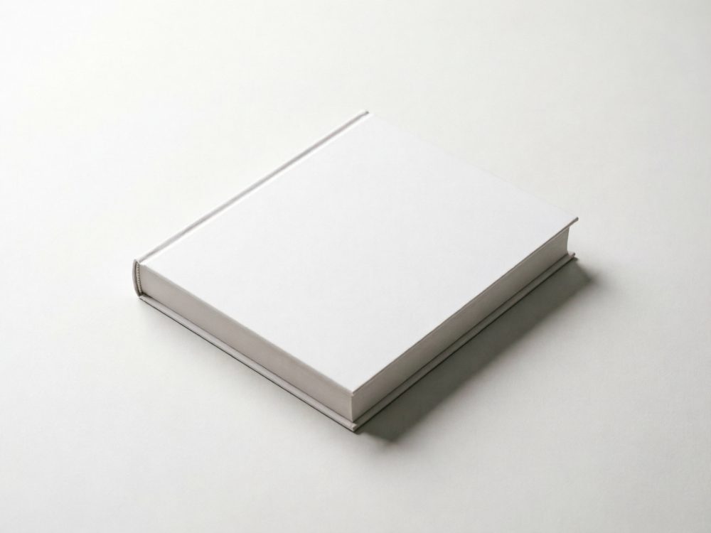 Livro com capa dura branca sob superfície branca num ambiente minimalista