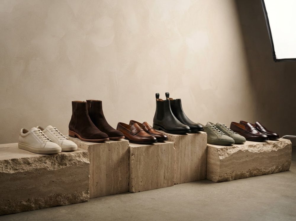Sapatos e botas masculinas de vários estilos exibidos sobre blocos de pedra em fundo bege neutro