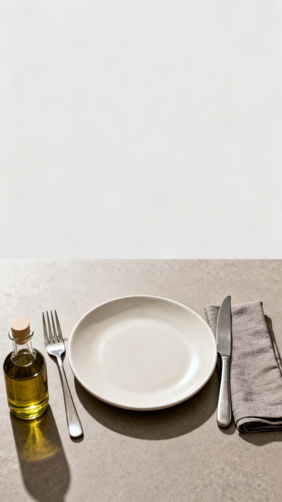 Mesa posta com prato branco, garfo à esquerda, faca e guardanapo cinza à direita e garrafa pequena de azeite