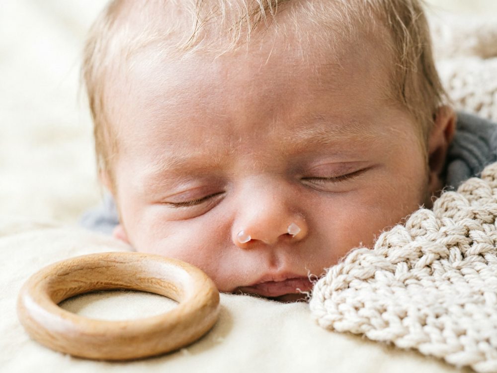 Bebé a dormir ao lado de anel de madeira e manta tricotada creme
