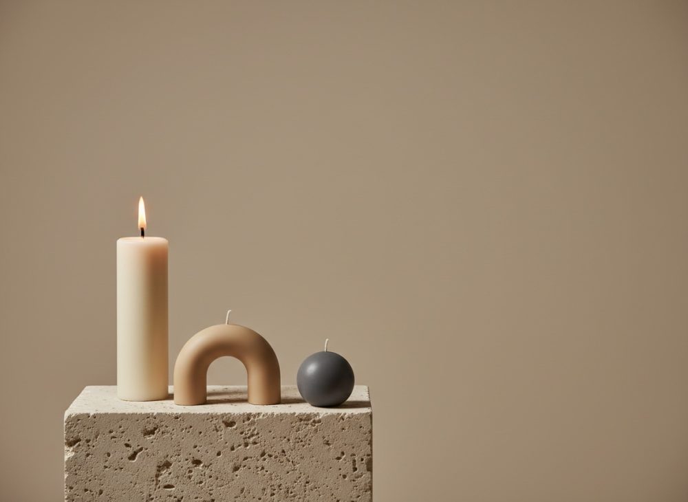 Trio de velas decorativas minimalistas em tons neutros sobre base de pedra com fundo bege