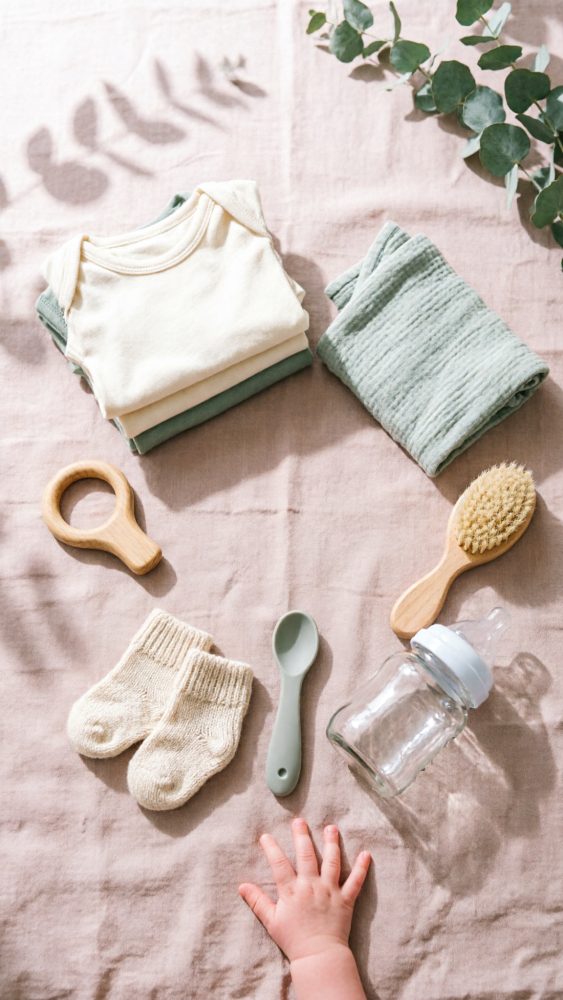 Conjunto de roupas e acessórios para bebé em tons neutros e mão pequena sobre tecido claro