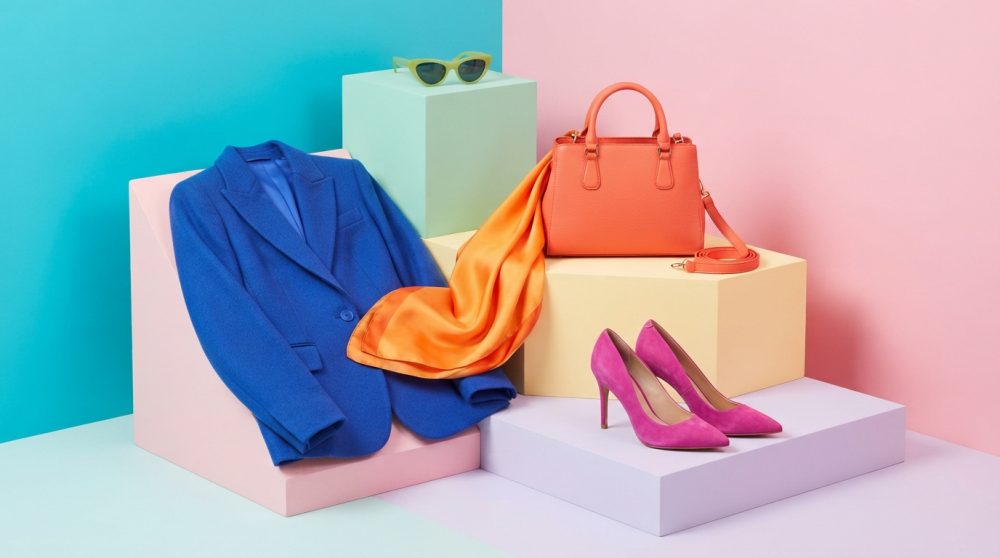Conjunto com blazer azul, lenço laranja, sapatos rosa, bolsa coral e óculos de sol em fundo colorido