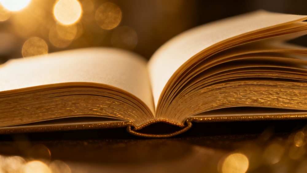 Livro aberto com páginas douradas iluminado por luz quente e fundo desfocado