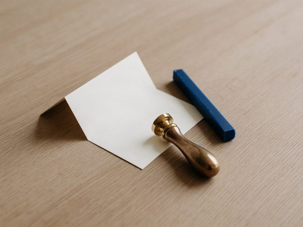 Envelope branco aberto com selo de cera dourado e bastão de cera azul sobre mesa de madeira