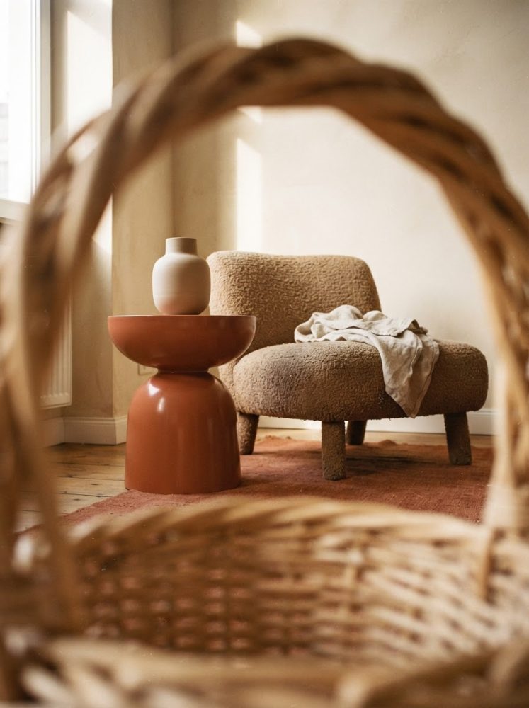 Poltrona creme felpuda com mesa terracota e vaso decorativo em ambiente iluminado naturalmente