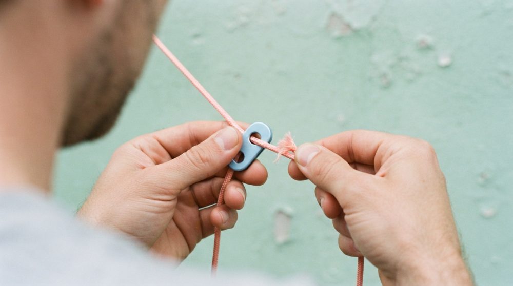 Mãos masculinas a ajustar corda coral num dispositivo cinzento com fundo verde