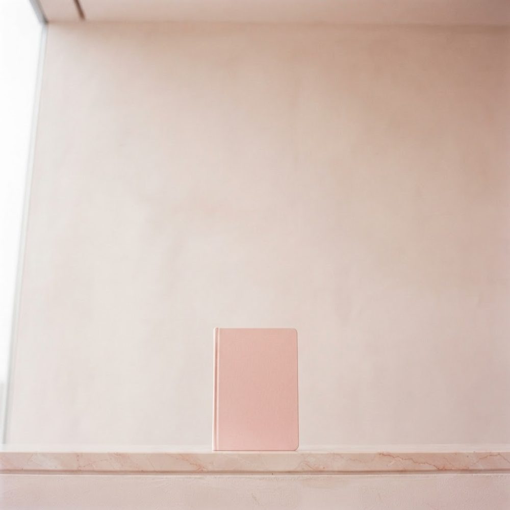 Caderno rosa em pé sobre mesa clara com fundo neutro e iluminação suave