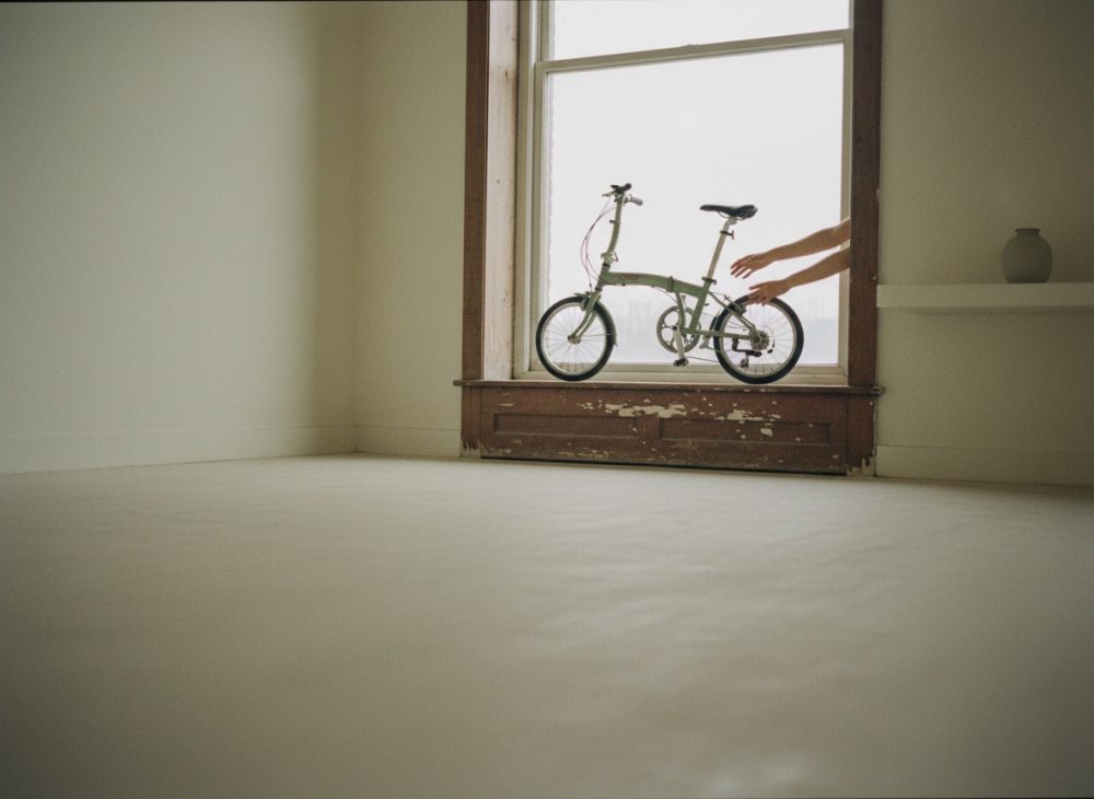 Bicicleta dobrável colocada no peitoril de uma janela com moldura de madeira envelhecida num espaço minimalista.