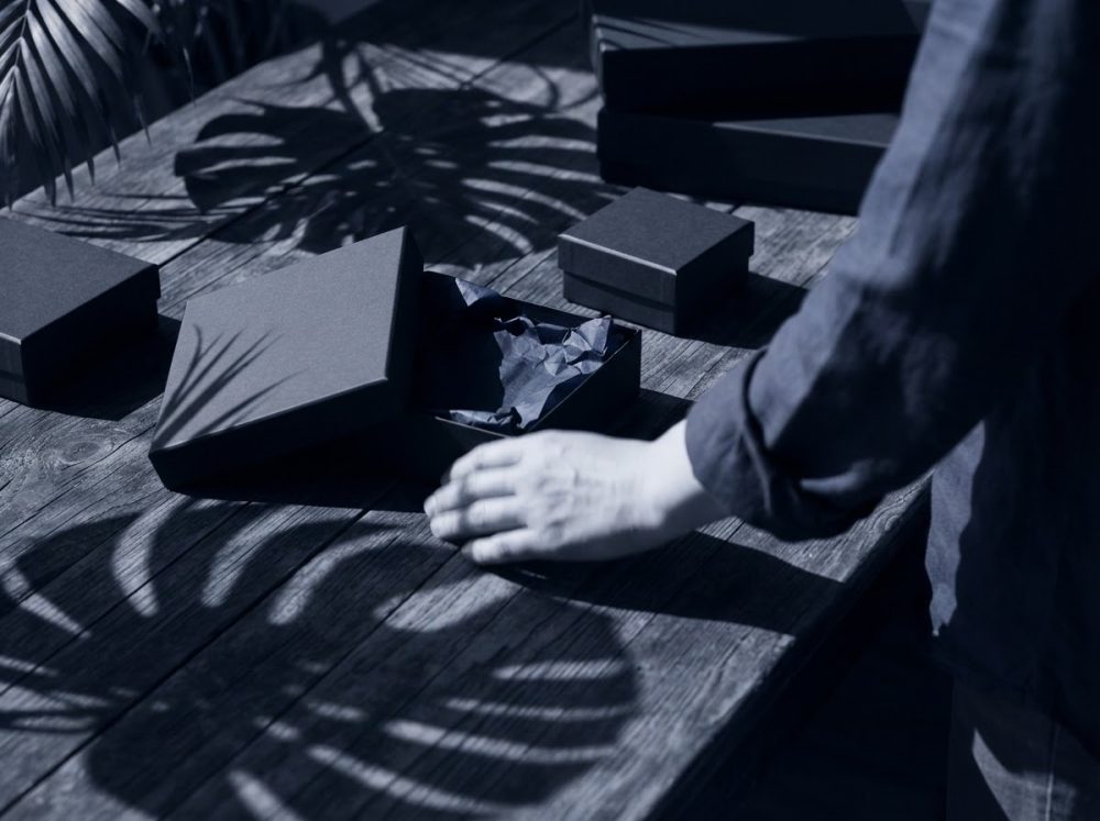 Caixas de presente pretas em mesa de madeira com sombras de folhas tropicais e mão masculina