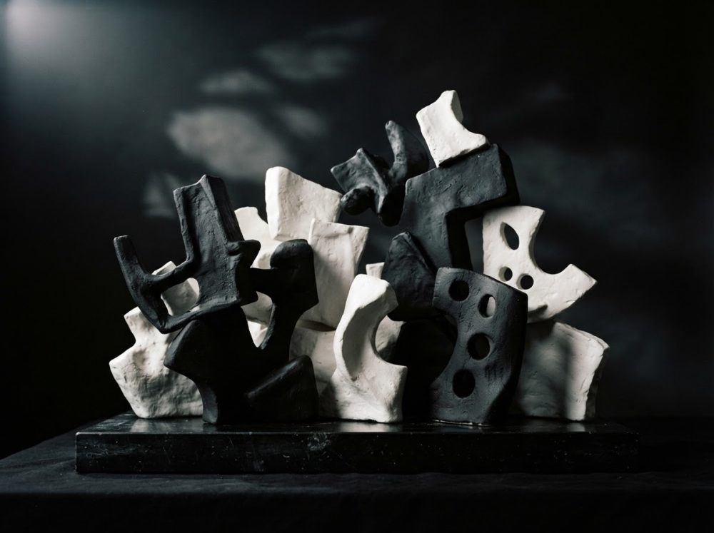 Escultura abstrata preta e branca com formas geométricas e recortes sobre base escura