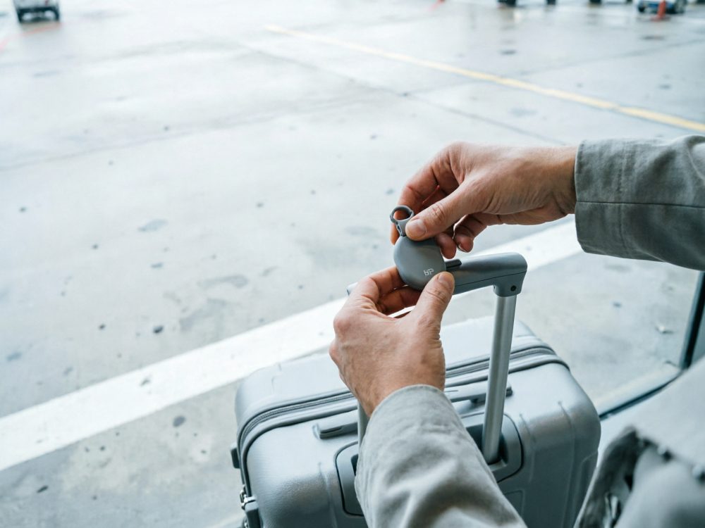Mãos segurando etiqueta cinzenta para mala cinzenta com pega extensível em aeroporto