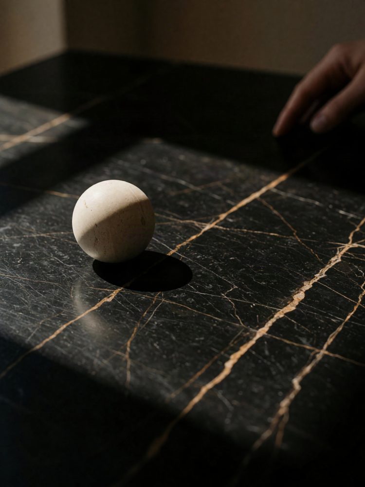 Mesa de mármore preto com veios dourados e esfera branca a destacar-se sob luz suave