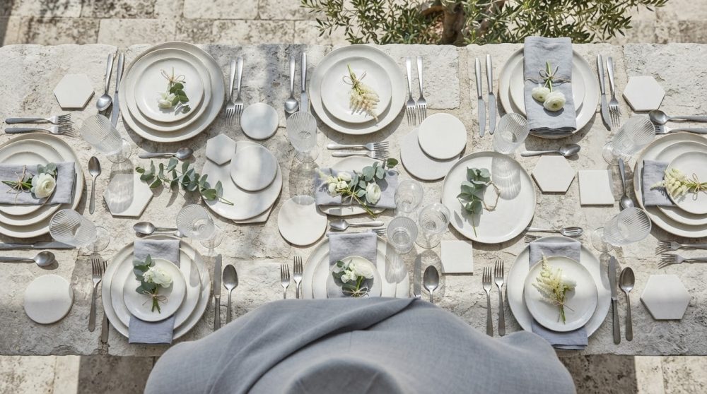 Mesa elegante com louça branca, talheres prateados e flores para casamento ao ar livre
