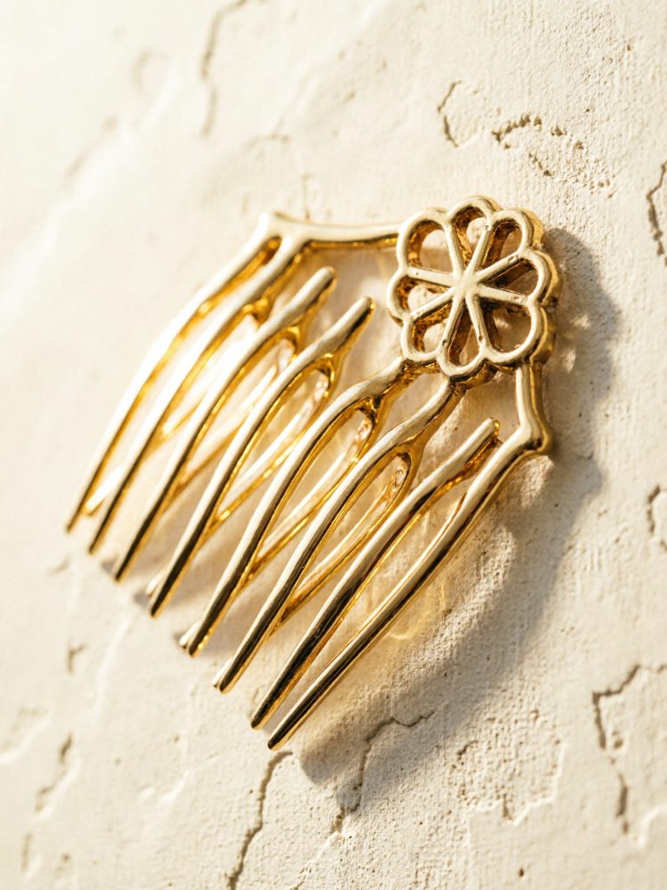 Pente de cabelo dourado com ornamento floral, apoiado numa parede clara texturada