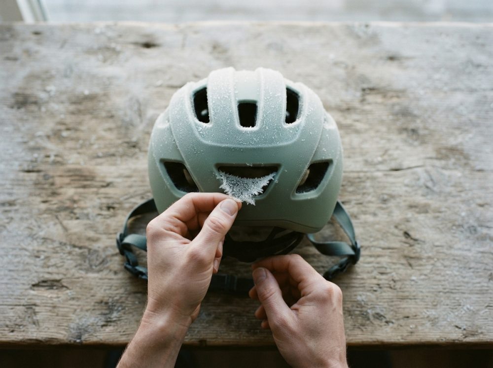 Mãos retirando geada de capacete de bicicleta sobre mesa de madeira