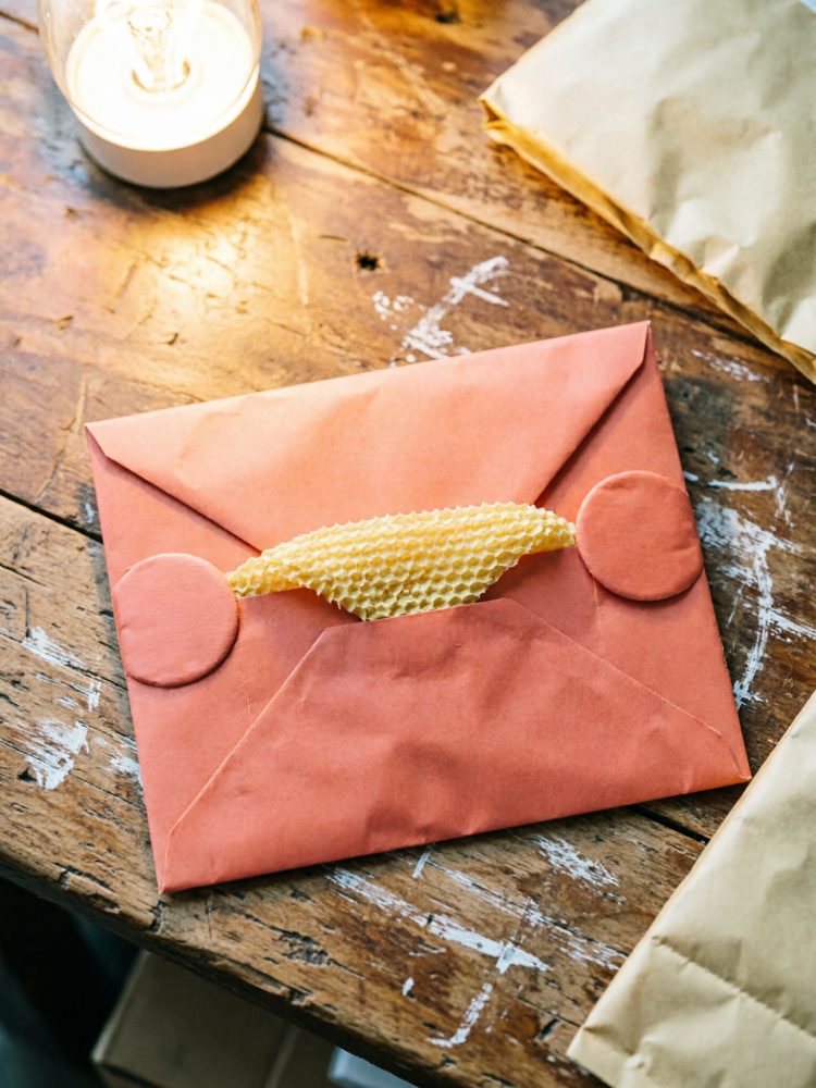 Envelope terracota de papel reciclado fechado com selos redondos sobre mesa de madeira rústica